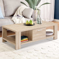 Light oak coffee table with one drawer and lower shelf in living room with sofa and plant