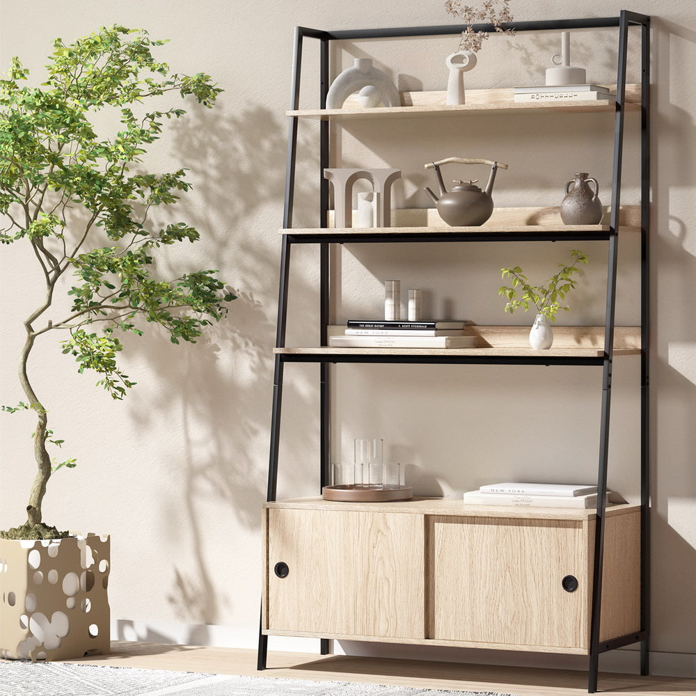 Oak and black metal ladder shelf with three open shelves above sliding door cabinet, styled with vases beside bonsai tree