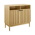 Natural oak reeded cabinet angled view, two open top compartments and two lower reeded doors with black handles, tapered legs