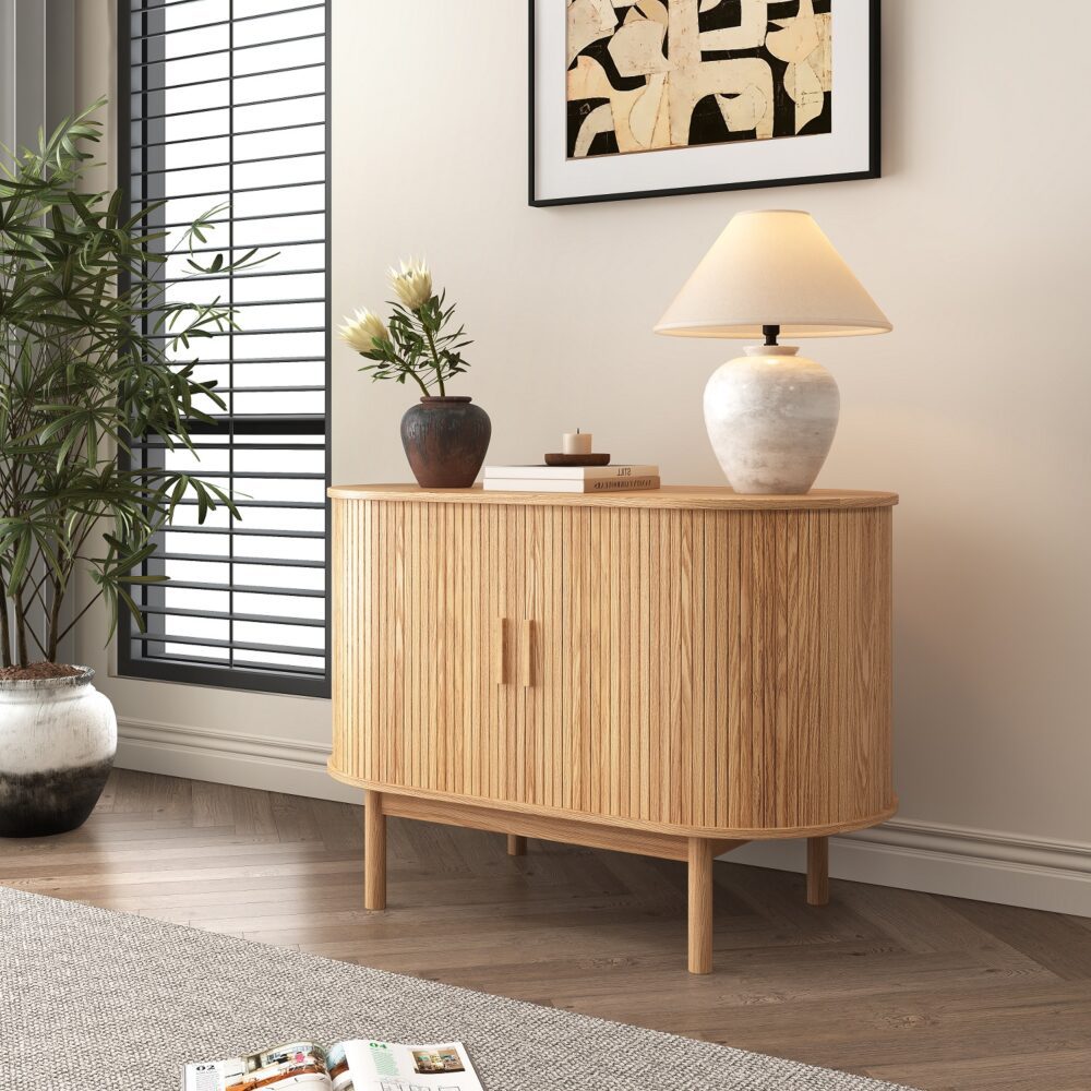Natural oak reeded sideboard in room setting with lamp, vase and candle on top, window blinds and framed art in background
