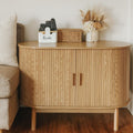 Oak reeded sideboard with rounded ends beside sofa, remote holder, wicker basket and dried flowers on top