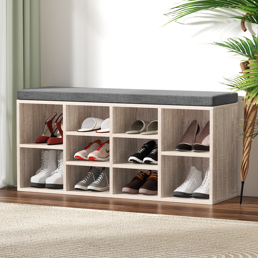 Oak shoe storage bench grey cushion 10 open cubbies loaded with heels boots and sneakers hallway lifestyle with plant and rug