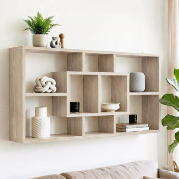 Natural oak wall-mounted display shelf with asymmetric grid compartments, styled with plants, ornaments and books