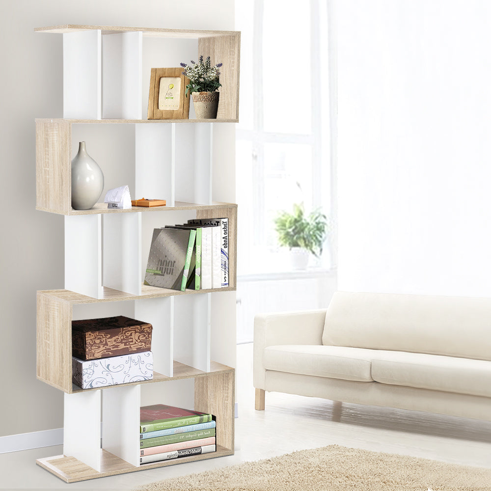 Oak and white S-shaped 5-tier display shelf in living room styled with books, vase and plant beside cream sofa