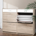 Oak and white shoe cabinet side by side with one upper flip-down compartment open showing slatted mechanism