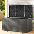 Large grey outdoor storage box with lid open showing ventilated interior, on timber patio with wicker furniture