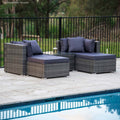 4-piece dark grey wicker outdoor set with navy cushions and glass coffee table on stone patio beside pool, trees behind fence