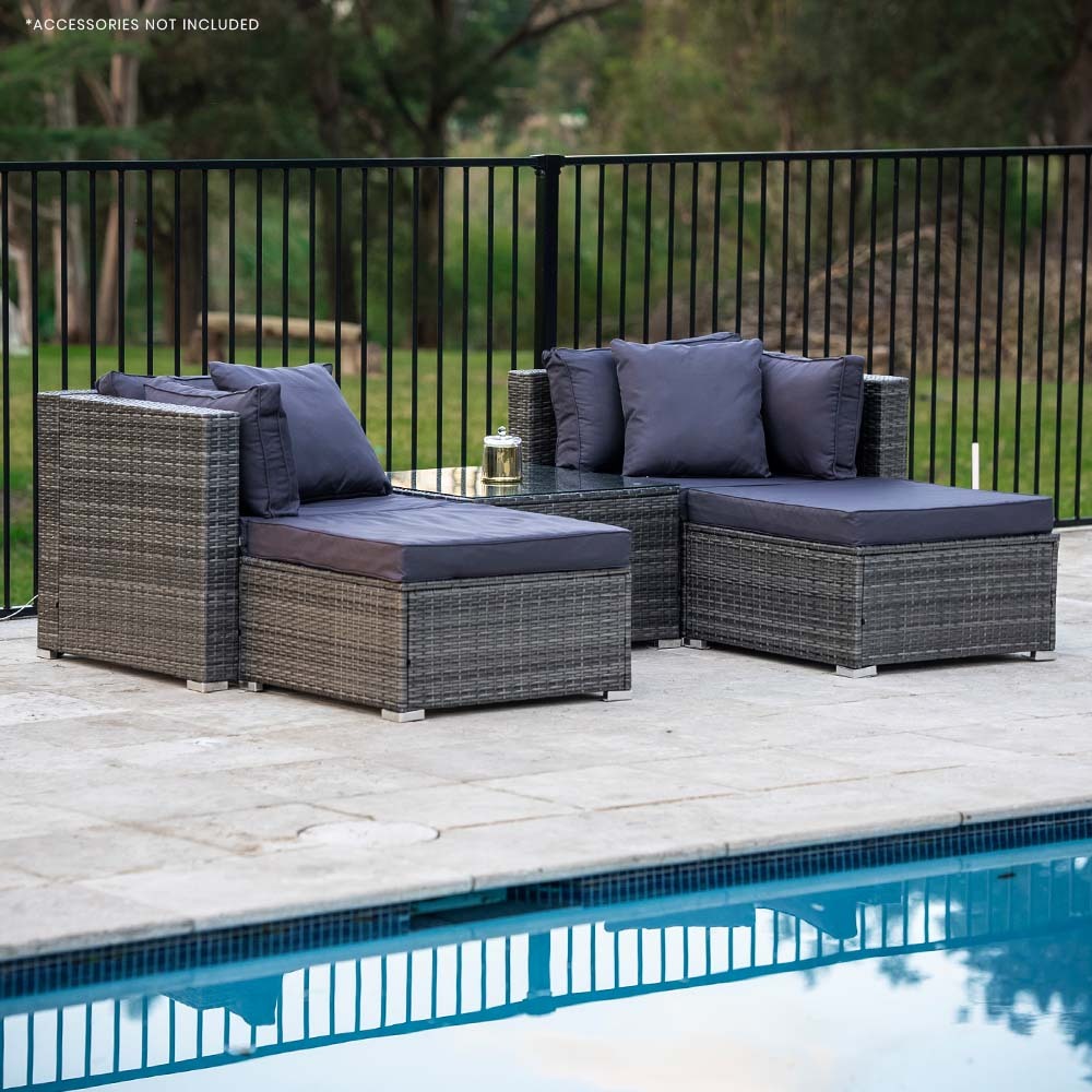 4-piece dark grey wicker outdoor set with navy cushions and glass coffee table on stone patio beside pool, trees behind fence