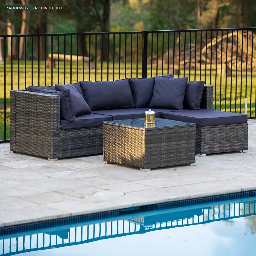 4-piece grey wicker outdoor sofa set with navy cushions in L-shape beside pool on stone patio, trees and fence in background