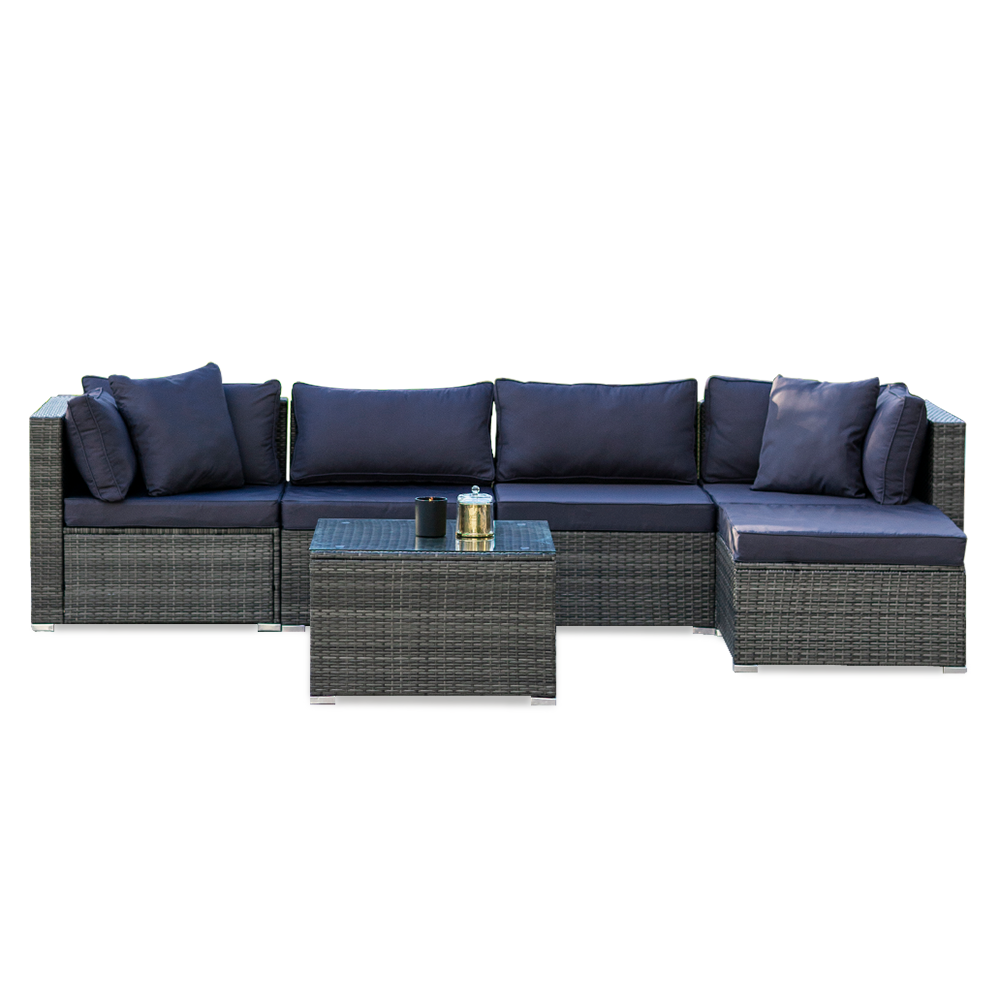 5-piece grey wicker outdoor sofa set with navy cushions in L-shape with chaise and glass coffee table, white background