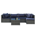 5-piece grey wicker outdoor sofa set with navy cushions in L-shape with chaise and glass coffee table, white background