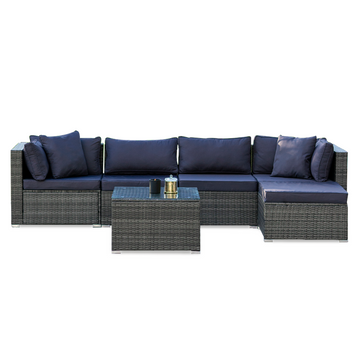 5-piece grey wicker outdoor sofa set with navy cushions in L-shape with chaise and glass coffee table, white background