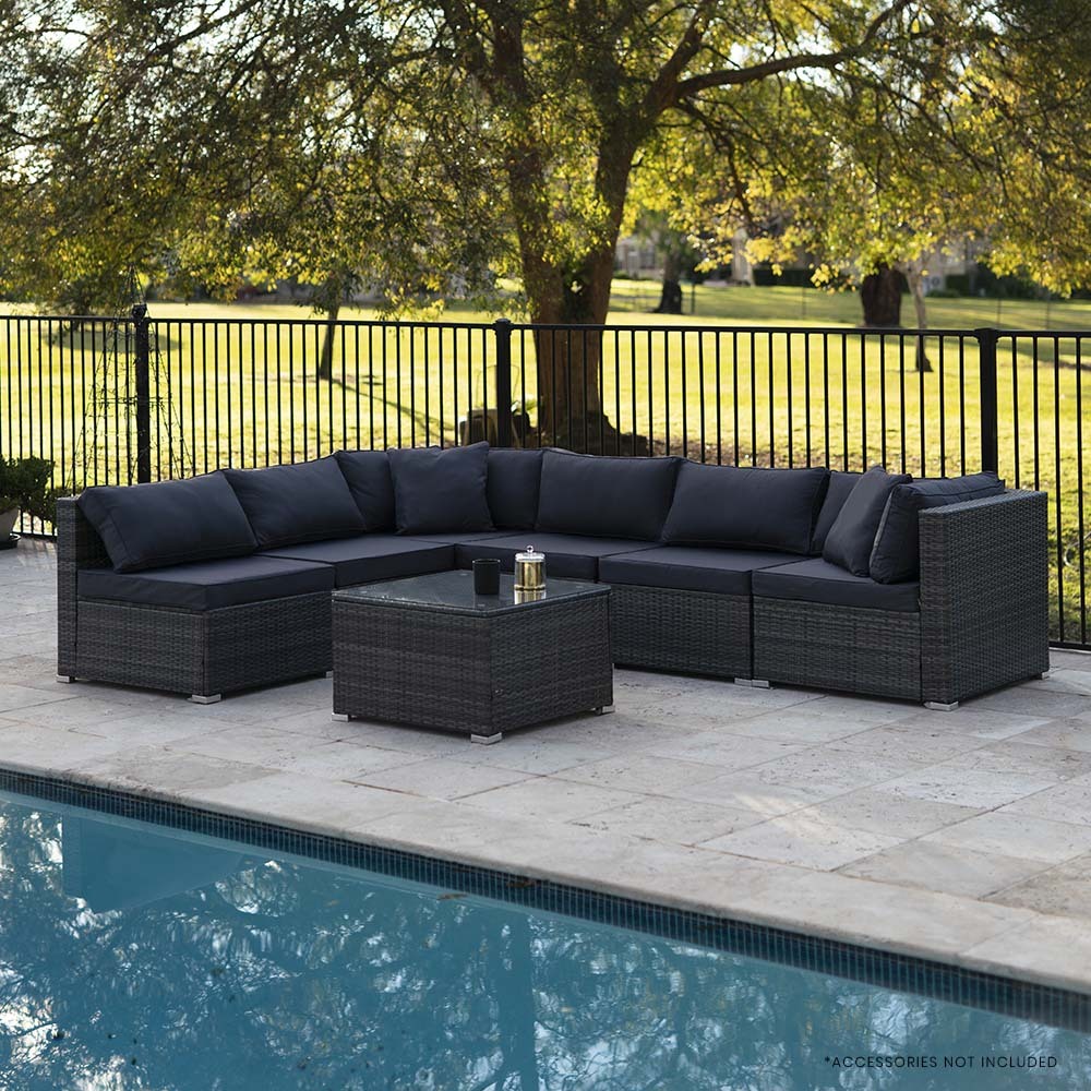 6-piece dark grey wicker sectional sofa with dark cushions in L-shape beside pool on stone patio, trees behind fence