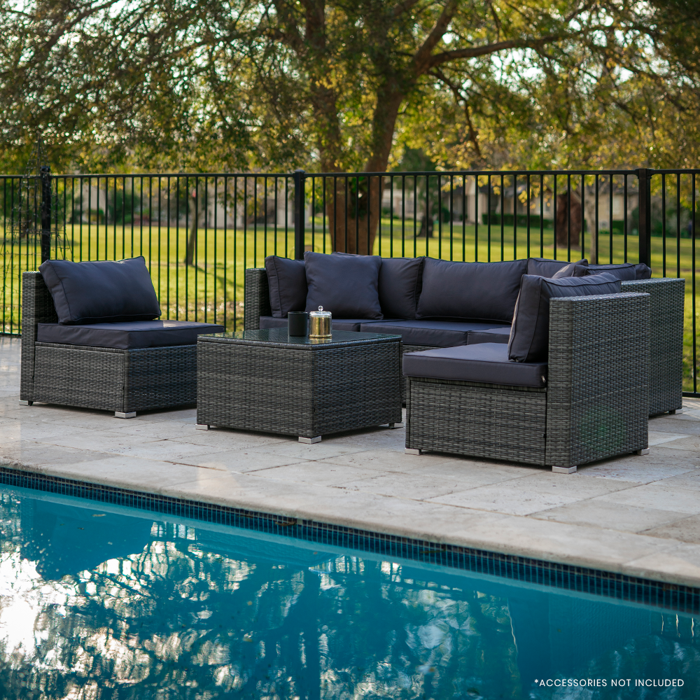 5-piece grey wicker outdoor sofa set with navy cushions arranged beside pool on stone patio with trees behind fence
