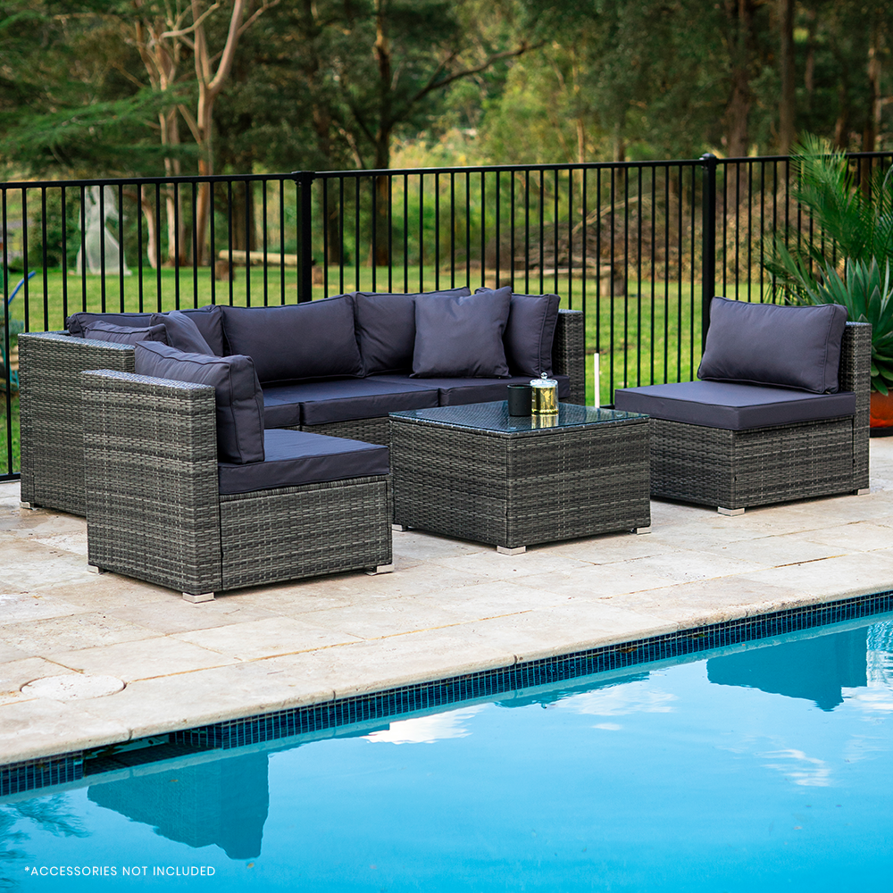 5-piece grey wicker outdoor sofa set with navy cushions beside pool on stone patio seen from angle view, trees in background