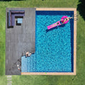 Aerial view of backyard pool with dark wood deck and wicker sofa set in corner, people visible by pool