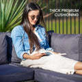 Woman in denim jacket seated on outdoor wicker sofa reading outdoors with text: Thick premium cushioning