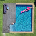 Aerial view of backyard pool with dark wood deck and wicker sofa set in corner, person on pink inflatable in pool