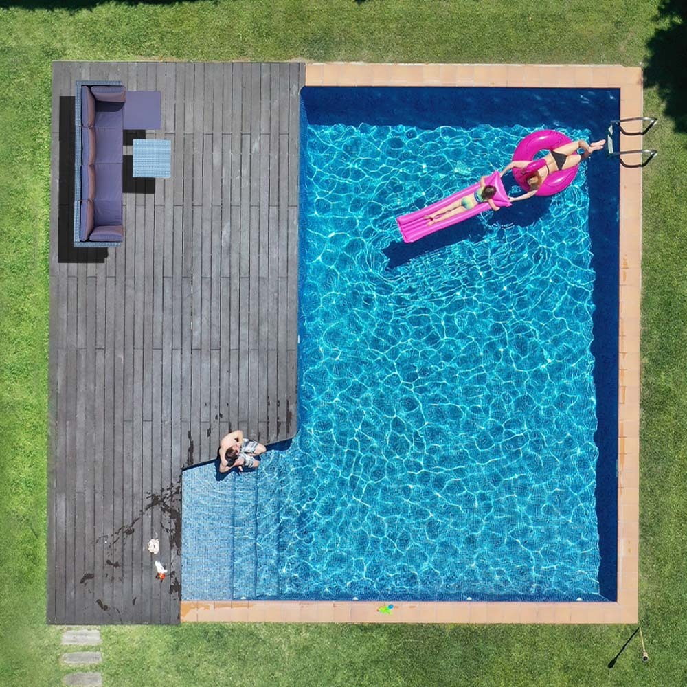 Aerial view of backyard pool with dark wood deck and wicker sofa set in corner, person on pink inflatable in pool
