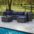5-piece dark grey wicker outdoor sofa set with navy cushions beside swimming pool on stone patio, trees behind fence