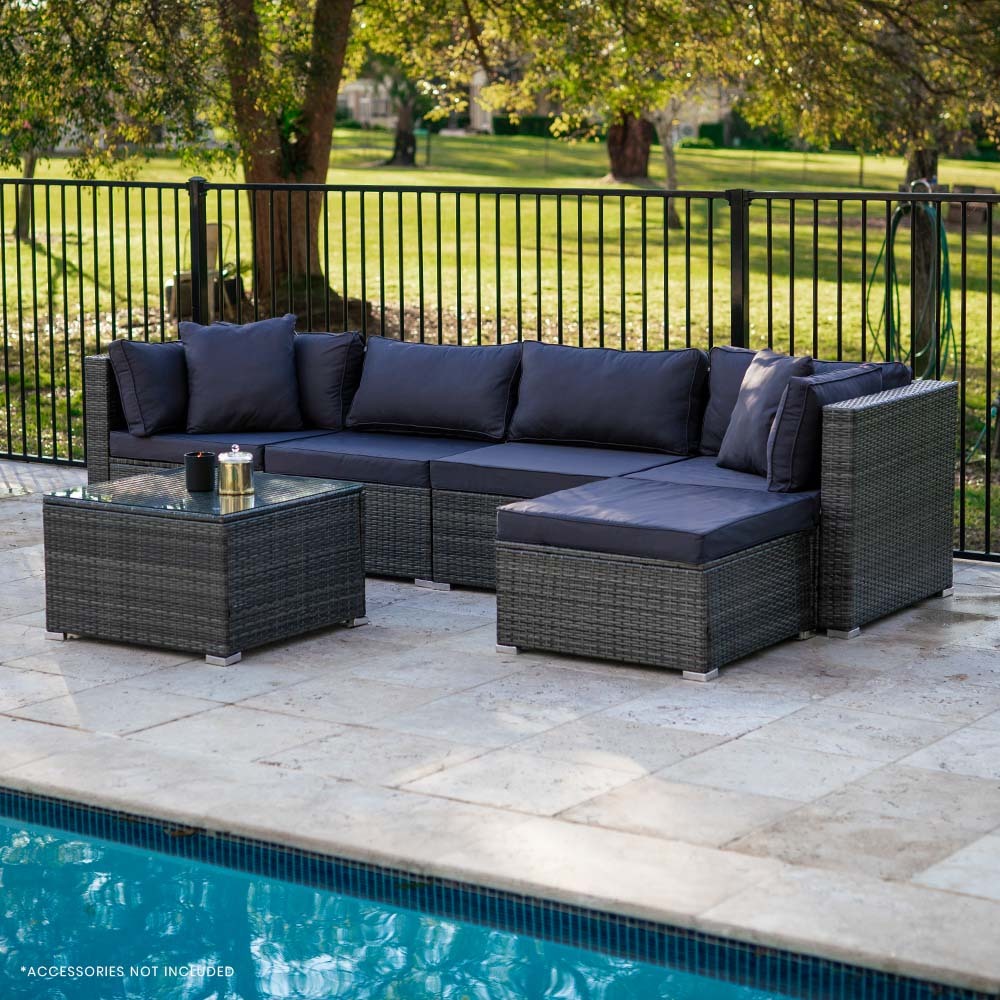 5-piece dark grey wicker outdoor sofa set with navy cushions beside swimming pool on stone patio, trees behind fence