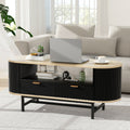 Oval coffee table with black fluted body, oak top, two drawers and open shelf, styled with laptop and plants in a living room