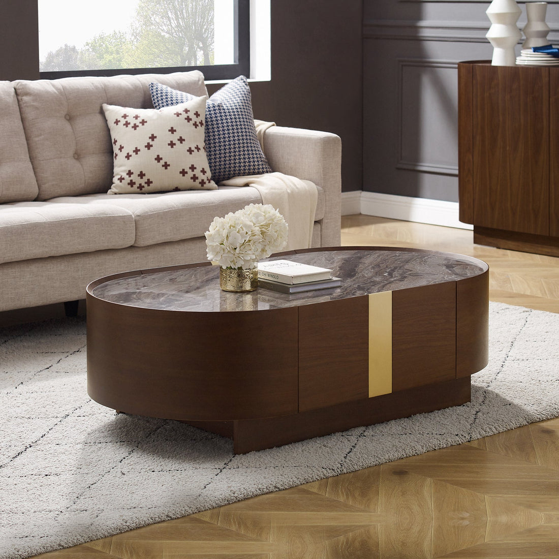 Oval coffee table with grey marble top, walnut wood base and brass vertical strip accent, styled in a living room with a
