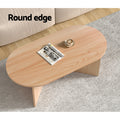 Top-down view of oval wood coffee table with round edge label, magazine and coffee cup placed on top