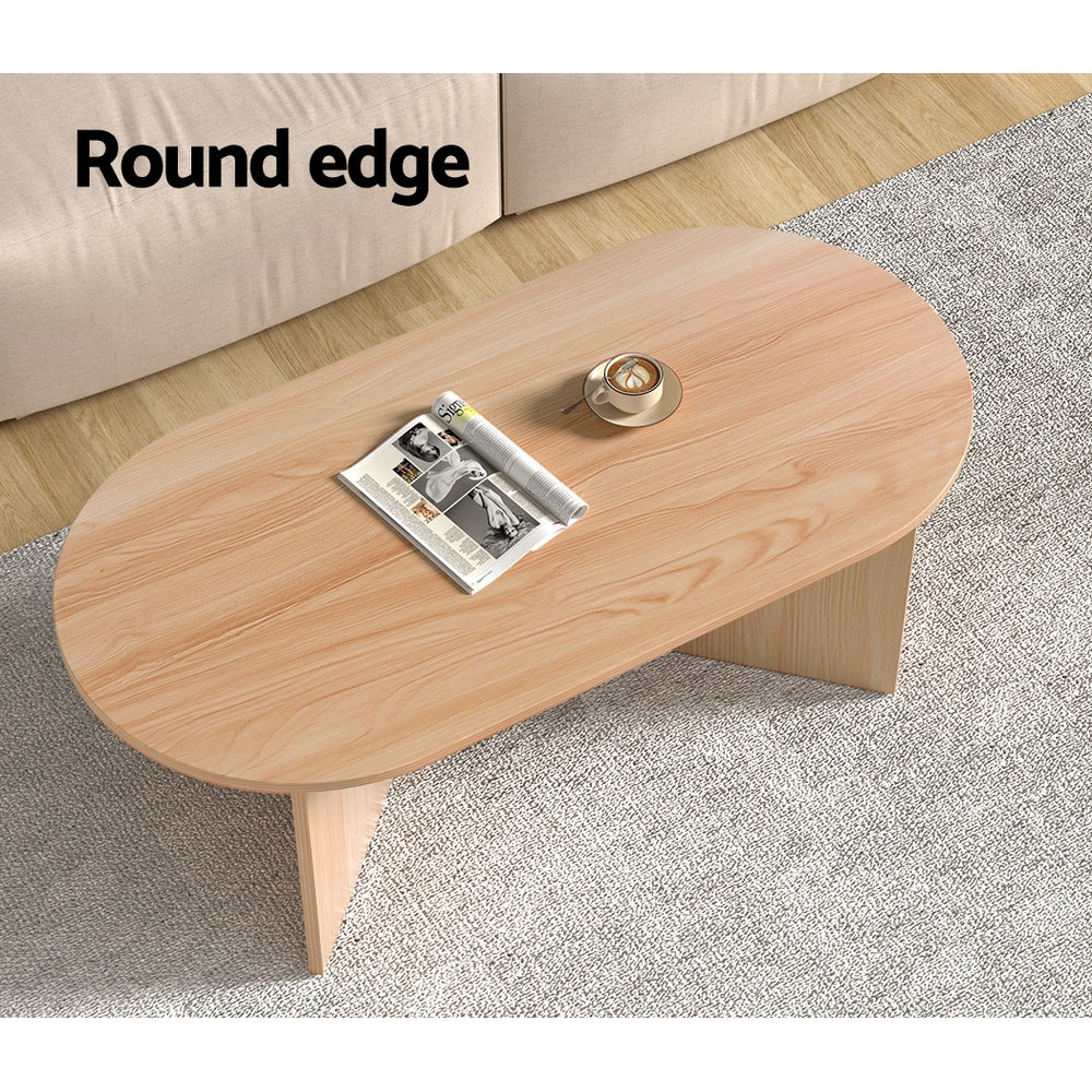 Top-down view of oval wood coffee table with round edge label, magazine and coffee cup placed on top