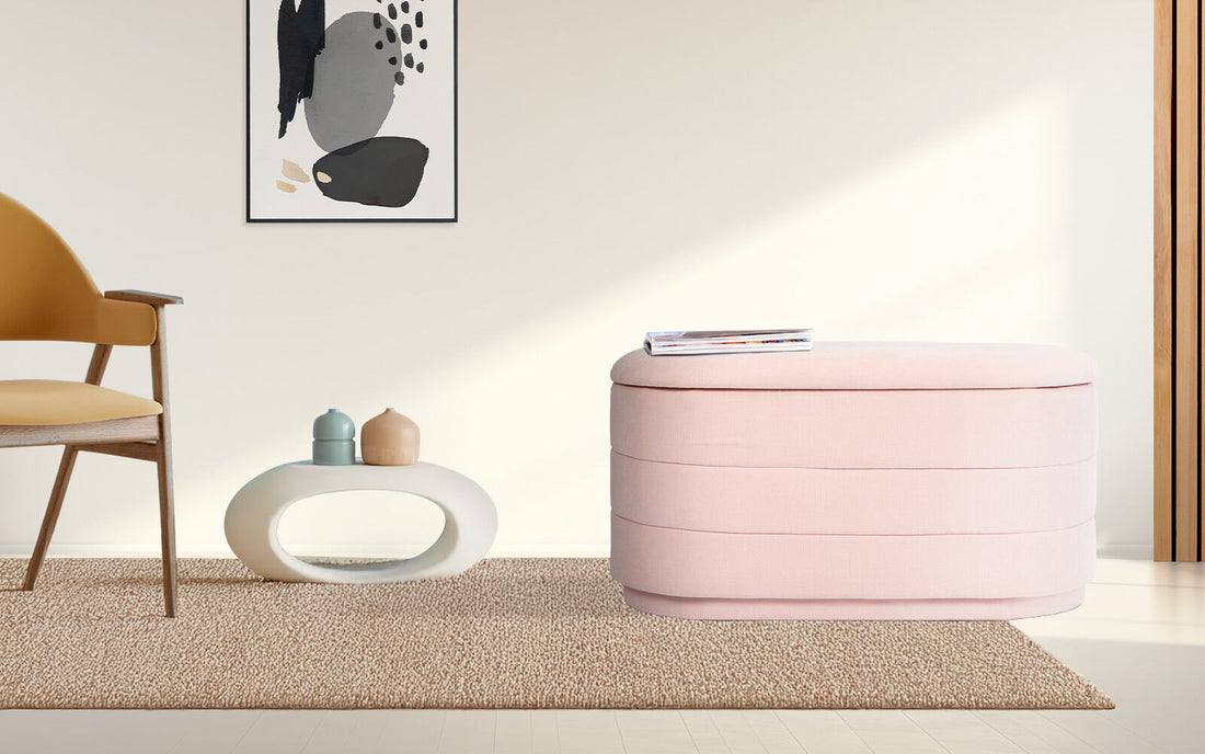 Oval pink fabric storage ottoman with horizontal channel stitching and natural wood grain lid on white background