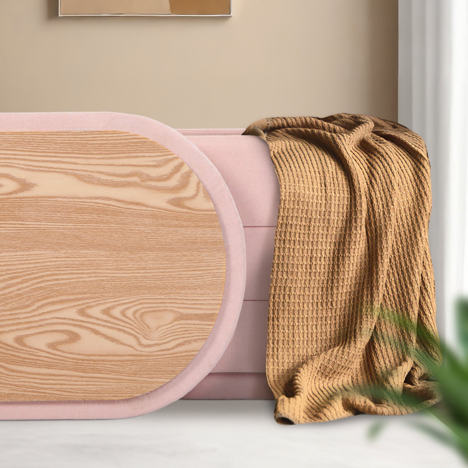 Oval wood grain lid leaning against pink fabric ottoman with tan waffle-knit throw draped over the side