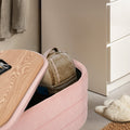 Pink storage ottoman with wood lid partly open showing tan backpack stored inside, fluffy slippers and dresser beside it