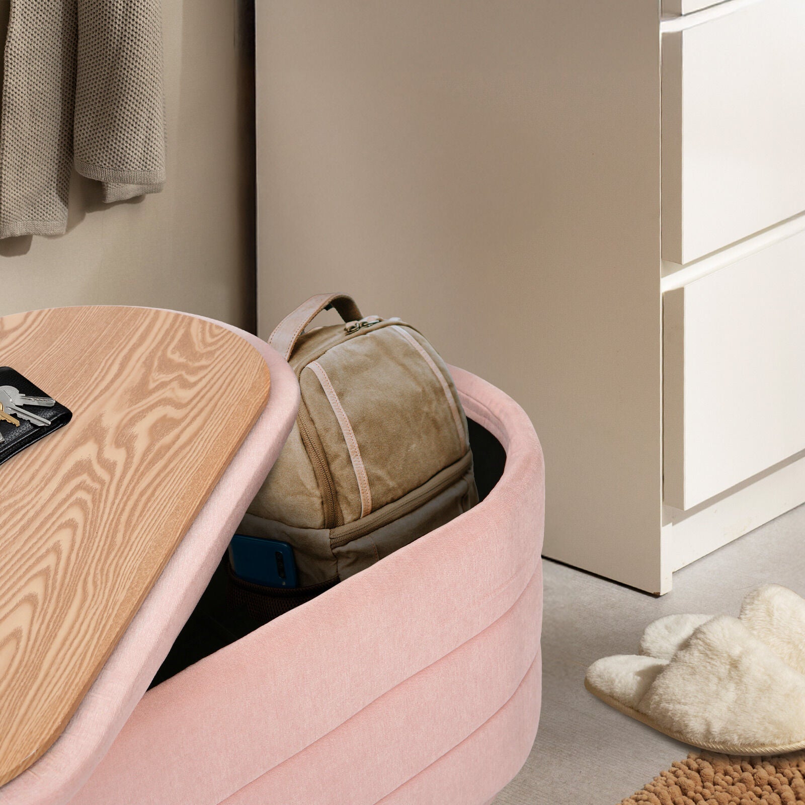 Pink storage ottoman with wood lid partly open showing tan backpack stored inside, fluffy slippers and dresser beside it