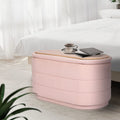 Pink fabric storage ottoman with wood lid at foot of white bed, coffee cup and books on top, sheer curtains in background
