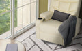 Cream PU leather recliner with tufted backrest, grey cushion and throw, cup holder, beside large window with garden view