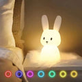 White rabbit night light on bedside table, 7 colour options shown: red, blue, purple, cyan, teal, yellow and warm