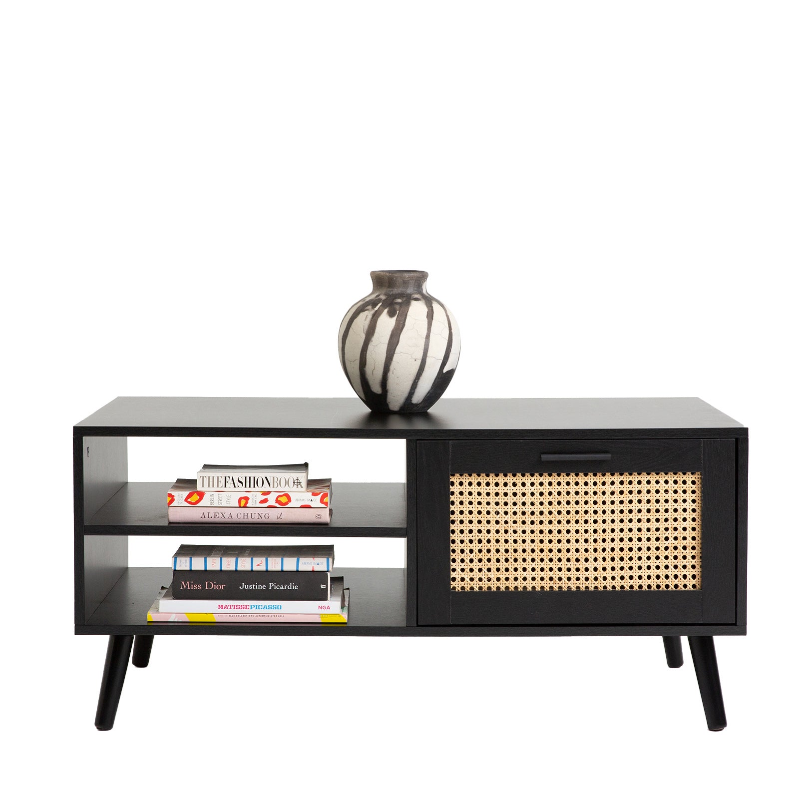 Black rattan coffee table with books stacked on open shelves and decorative vase on top, white background
