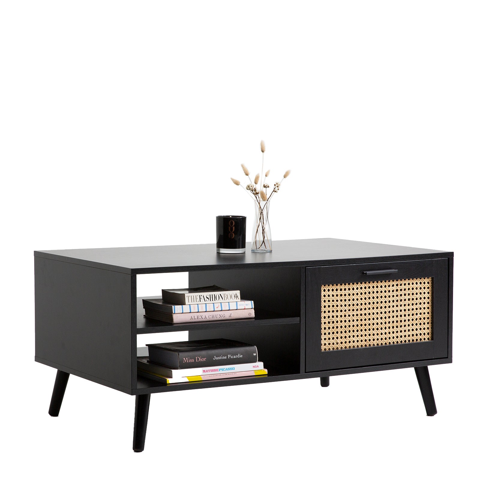 Black rattan coffee table styled with books on shelves, black candle and dried flower vase on top, white background