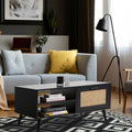 Black rattan coffee table with books on shelves in front of grey sofa with yellow cushion, black floor lamp and geometric rug