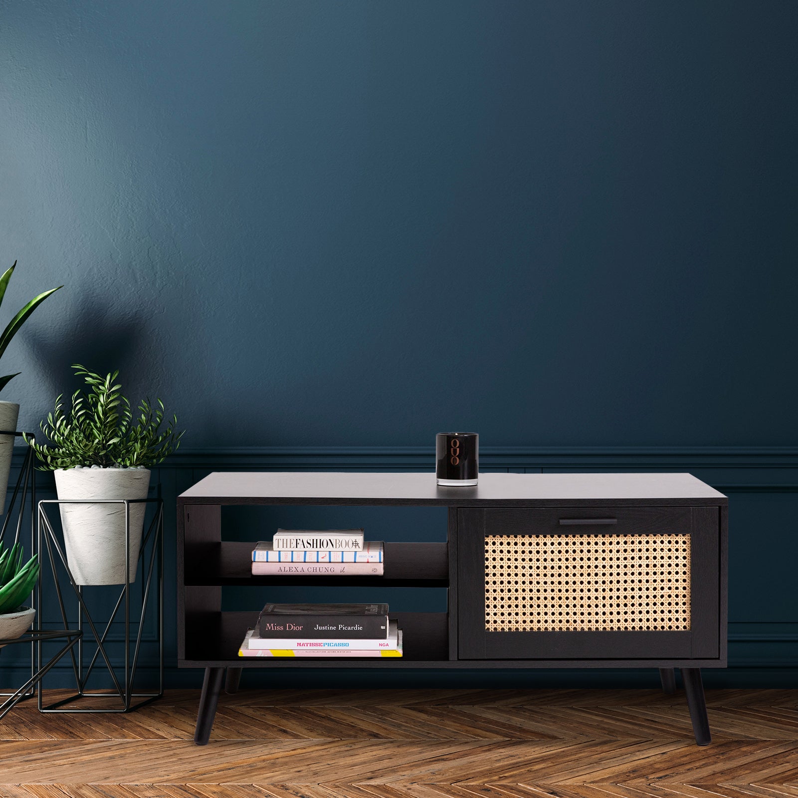 Black rattan coffee table against teal wall with books on shelves, small speaker on top and potted plant beside