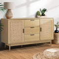 Natural wood and rattan sideboard with two cane doors and three drawers, styled with lamp and plants in living room
