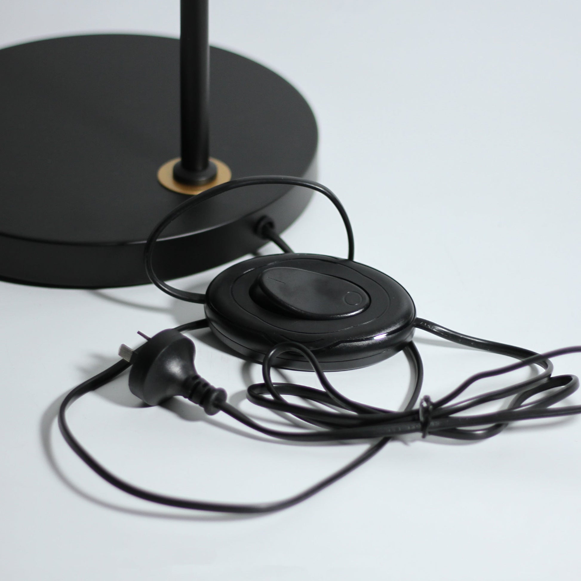 Black round floor lamp base with black cord, oval foot switch and Australian three-pin plug on white surface
