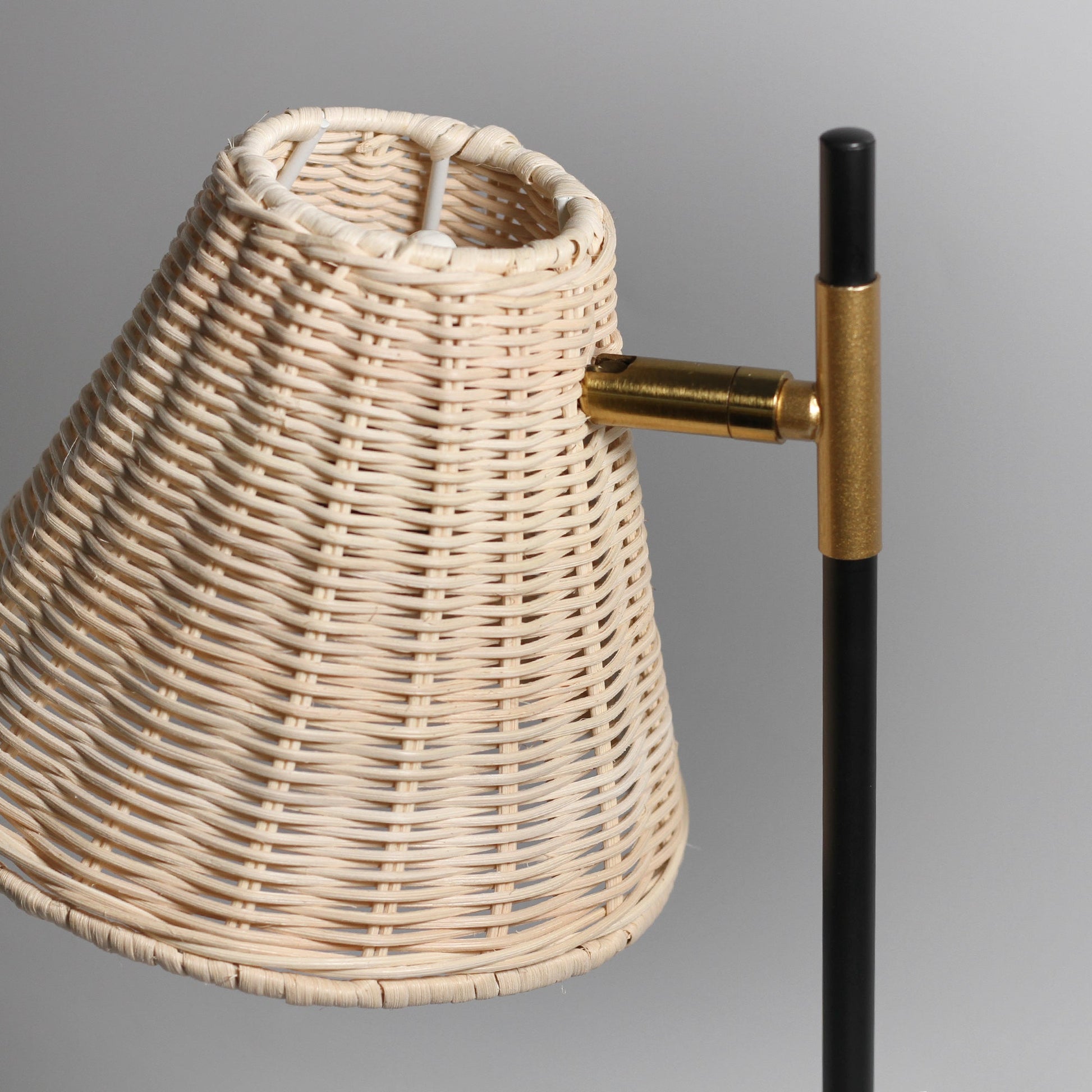 Close-up of woven rattan lampshade tilted on brass pivot connector with black pole, showing intricate weave texture