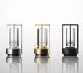 Three retro lantern LED table lamps in silver, gold and black with cylindrical glass tubes on white background
