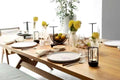 Black retro lantern LED lamp on set wooden dining table with plates, cutlery, glassware and yellow flower vases
