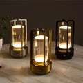 Three retro lantern LED table lamps in silver, gold and black glowing on marble table with plant in background