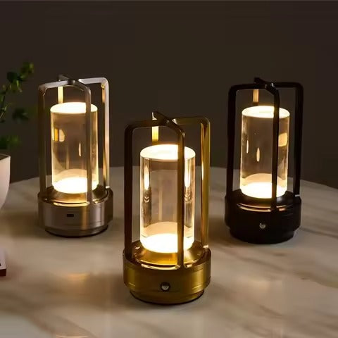 Three retro lantern LED table lamps in silver, gold and black glowing on marble table with plant in background
