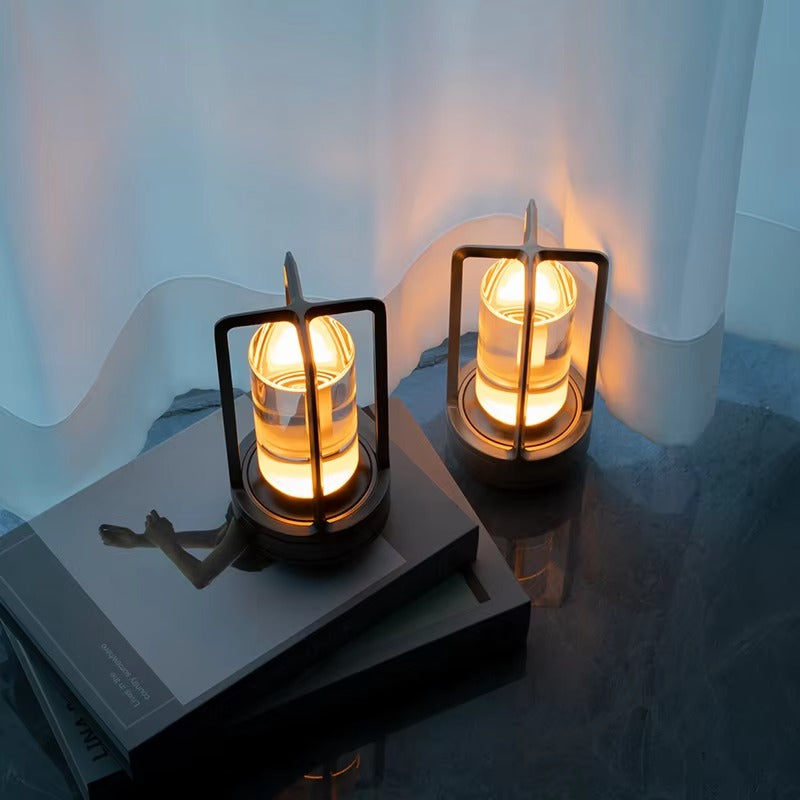 Two black retro lantern LED lamps glowing amber on dark coffee table books against white sheer curtain backdrop