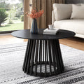 Black round coffee table with slatted pedestal base styled in a living room with a vase of flowers, books and coffee cup on