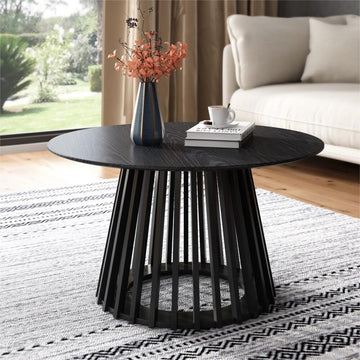 Black round coffee table with slatted pedestal base styled in a living room with a vase of flowers, books and coffee cup on